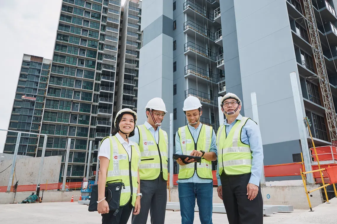 A site inspection team in high-visibility vests and hard hats reviews plans on a tablet in front of a residential condominium tower under construction in Singapore
